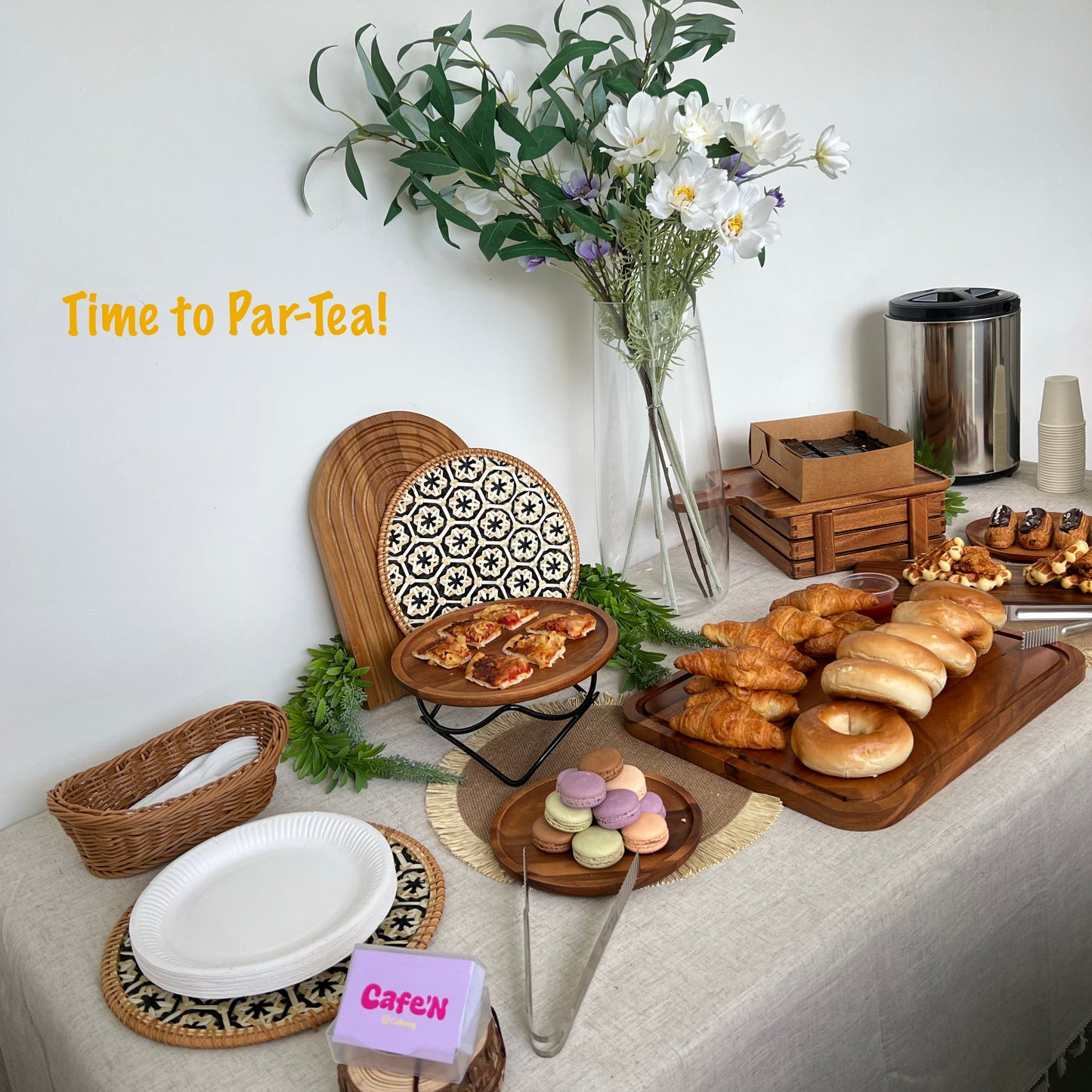 Café'N tea time setup with pastries, cookies, and flowers on a table.